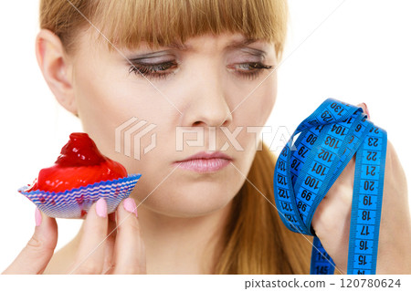 Woman holds cupcake trying to resist temptation 120780624