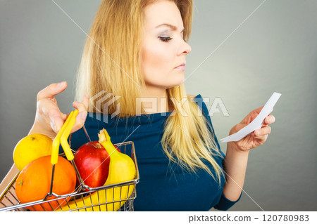 Worried woman holding shopping basket with fruits 120780983
