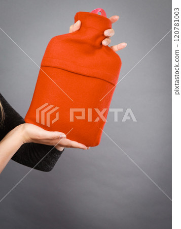 Woman holds hot water bottle in red fleece cover 120781003