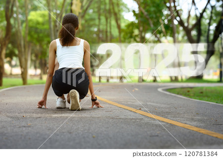 Chasing Goals in 2025. Young woman crouching in a starting position on paved path with the number 2025 120781384