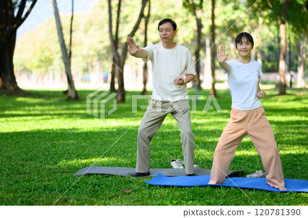 Middle aged father and daughter practicing Tai Chi in serene park. Family activities, health and well being concept 120781390