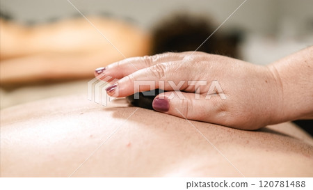 Massage therapist placing hot stone on client's back during spa treatment 120781488