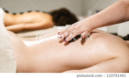 Masseuse placing hot stone on client's back during spa treatment Masseuse placing hot stone on client's back during spa treatment 120781491