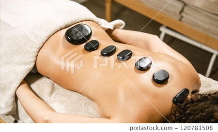 Masseur placing hot stones on woman's back during spa treatment Masseur placing hot stones on woman's back during spa treatment 120781508