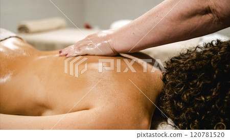 Masseuse applying oil on woman's back during relaxing massage therapy session 120781520