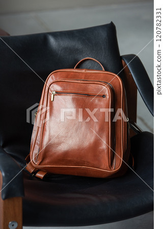Brown leather backpack on the stylish chair 120782331