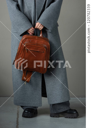 woman posing with a leather backpack wearing a warm gray coat and black boots woman posing with a leather backpack wearing a warm gray coat and black boots 120782339