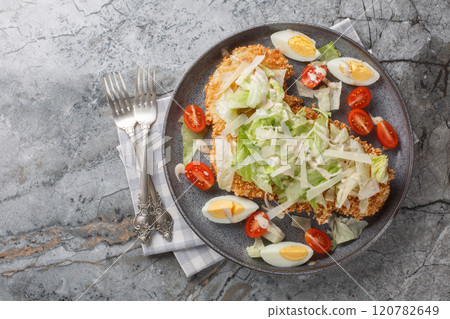 Chicken Caesar salad with crispy schnitzel, boiled eggs, parmesan, iceberg lettuce and tomatoes closeup on the plate. Horizontal top view Chicken Caesar salad with crispy schnitzel, boiled eggs, parmesan, iceberg lettuce and tomatoes closeup on the plate. Horizontal top view 120782649