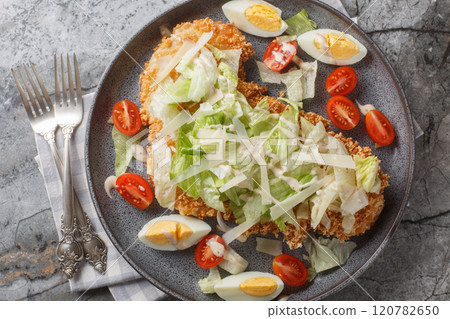 Delicious fresh schnitzel caesar salad with chicken meat, eggs, parmesan, iceberg lettuce and tomatoes close-up in a plate. Horizontal top view Delicious fresh schnitzel caesar salad with chicken meat, eggs, parmesan, iceberg lettuce and tomatoes close-up in a plate. Horizontal top view 120782650