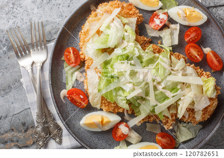 Breaded schnitzel Caesar salad with crispy chicken meat, eggs, parmesan, iceberg lettuce and tomatoes close-up in a plate. horizontal top view Breaded schnitzel Caesar salad with crispy chicken meat, eggs, parmesan, iceberg lettuce and tomatoes close-up in a plate. horizontal top view 120782651
