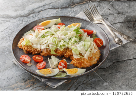 Breaded schnitzel Caesar salad with crispy chicken meat, eggs, parmesan, iceberg lettuce and tomatoes close-up in a plate. horizontal 120782655
