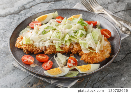 Chicken Caesar salad with crispy schnitzel, boiled eggs, parmesan, iceberg lettuce and tomatoes closeup on the plate. Horizontal 120782656
