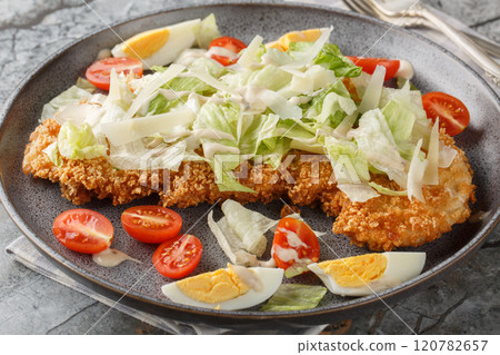 Delicious fresh schnitzel caesar salad with chicken meat, eggs, parmesan, iceberg lettuce and tomatoes close-up in a plate. Horizontal 120782657