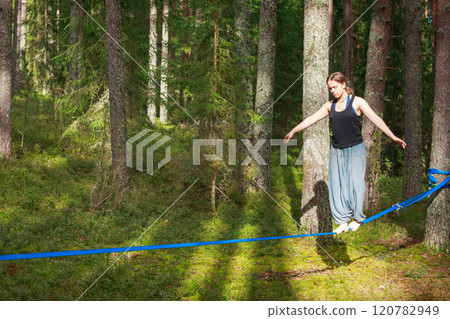 Teenage girl balancing on a slackline in the forest 120782949