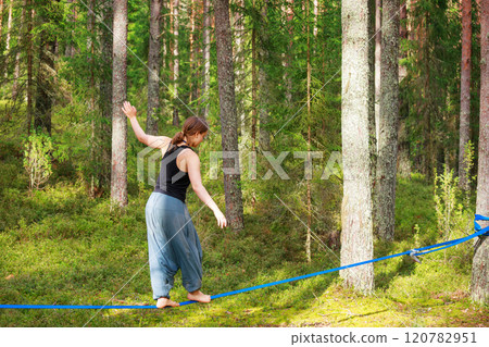 Teenage girl balancing on a slackline in the forest Teenage girl balancing on a slackline in the forest 120782951