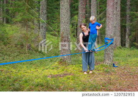 Teenage girl helping a young boy balance on a slackline in the forest 120782953