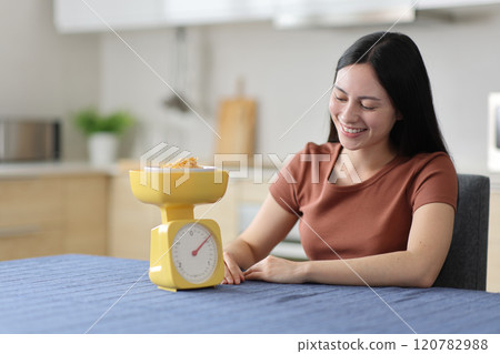 Happy asian woman weighing cereals in the kitchen 120782988
