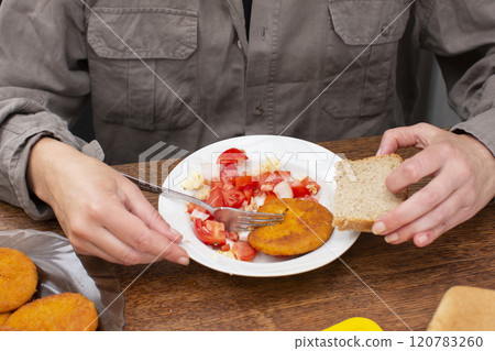 An unrecognizable man eats food from a plate. 120783260
