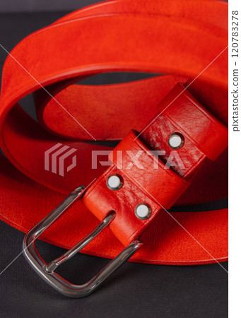 The piece is a red leather belt with a metal buckle beautifully curved on a gray background. 120783278