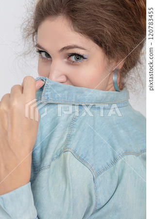Close-up portrait of a young girl covering her face with a denim shirt. Close-up portrait of a young girl covering her face with a denim shirt. 120783455