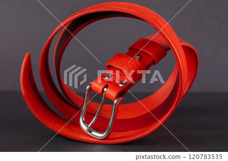 A red leather belt with a metal buckle beautifully curved on a gray background. A red leather belt with a metal buckle beautifully curved on a gray background. 120783535