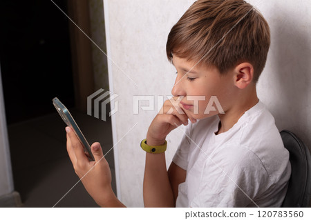 A teenage boy sits with a smartphone at home. A teenage boy sits with a smartphone at home. 120783560