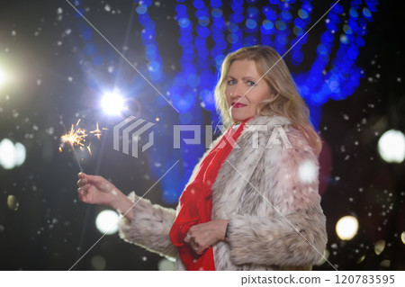 Portrait of a beautiful woman with a sparkler in an illuminated evening city. Happy evening celebration moment. Portrait of a beautiful woman with a sparkler in an illuminated evening city. Happy evening celebration moment. 120783595