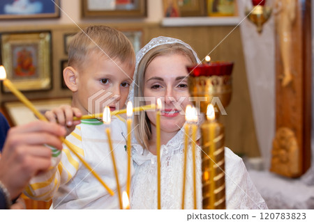 A mother and her little son light a candle at the altar in church. 120783823