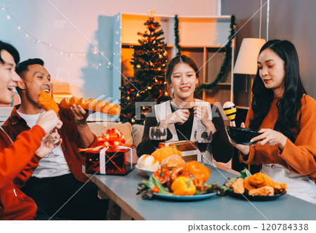 Group of young Asian man and women as friends having fun at a New Year's celebration, holding gift boxes standing by Christmas tree decoration, midnight countdown Party at home with holiday season. Group of young Asian man and women as friends having fun at a New Year's celebration, holding gift boxes standing by Christmas tree decoration, midnight countdown Party at home with holiday season. 120784338