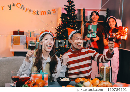Group of happy Asian friends celebrating Christmas and decorate the Christmas tree indoors. Beauty woman with Christmas Gifts. New Year party. Woman hands decorate Christmas tree red ball, bauble. 120784391