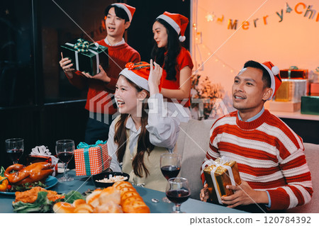 Group of happy Asian friends celebrating Christmas and decorate the Christmas tree indoors. Beauty woman with Christmas Gifts. New Year party. Woman hands decorate Christmas tree red ball, bauble. 120784392
