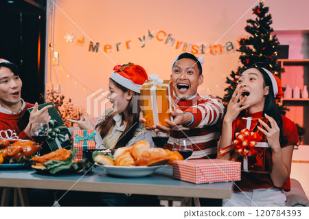 Group of happy Asian friends celebrating Christmas and decorate the Christmas tree indoors. Beauty woman with Christmas Gifts. New Year party. Woman hands decorate Christmas tree red ball, bauble. 120784393