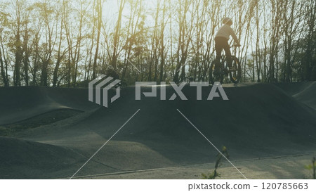 Unknown kids and ride their bikes fast on a pumptrack or pump track at sunset Unknown kids and ride their bikes fast on a pumptrack or pump track at sunset 120785663