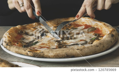 An elegant woman cuts freshly cooked hot pizza on her plate 120785669