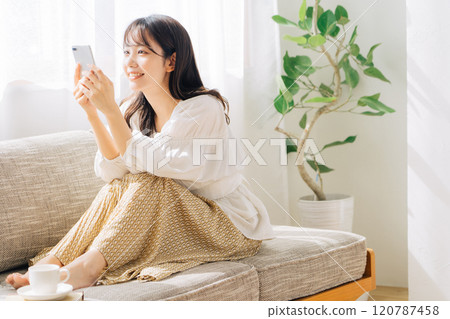 Woman sitting on a sofa and looking at a smartphone Woman sitting on a sofa and looking at a smartphone 120787458