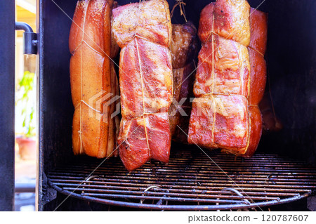 Smoker containing various cuts of bacon hung from hooks racks combine to create culinary tradition great enjoyment in smokehouse Smoker containing various cuts of bacon hung from hooks racks combine to create culinary tradition great enjoyment in smokehouse 120787607