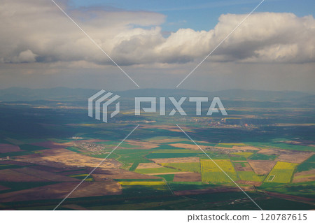 The landscape showcases vibrant green fields and patches of farmland, interspersed with low hills beneath a partly cloudy sky, illustrating the beauty of rural scenery. 120787615