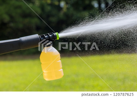Sprayer nozzle expels stream of liquid onto lush green grass in garden, promoting healthy plant growth 120787625