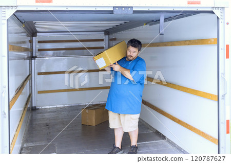 Man is lifting cardboard box while inside an empty moving truck features interior boxes are visible. Man is lifting cardboard box while inside an empty moving truck features interior boxes are visible. 120787627