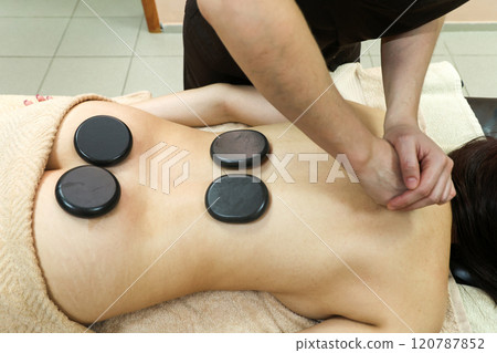 A Relaxing Back Massage with Heated Basalt Stones, Providing Deep Muscle Relief and Soothing Warmth to Enhance the Overall Spa Experience, Promoting Stress Reduction and Inviting Tranquility in a A Relaxing Back Massage with Heated Basalt Stones, Providing Deep Muscle Relief and Soothing Warmth to Enhance the Overall Spa Experience, Promoting Stress Reduction and Inviting Tranquility in a 120787852
