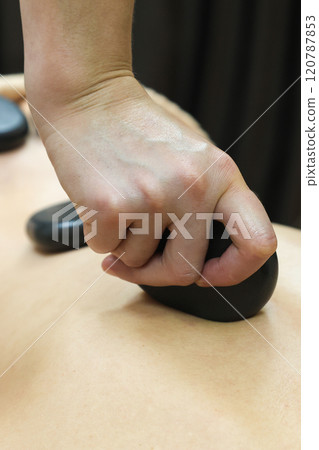 A Relaxing Back Massage with Heated Basalt Stones, Providing Deep Muscle Relief and Soothing Warmth to Enhance the Overall Spa Experience, Promoting Stress Reduction and Inviting Tranquility in a A Relaxing Back Massage with Heated Basalt Stones, Providing Deep Muscle Relief and Soothing Warmth to Enhance the Overall Spa Experience, Promoting Stress Reduction and Inviting Tranquility in a 120787853