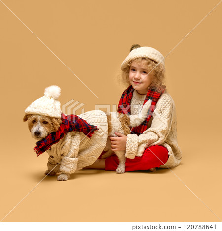 Beautiful little girl, child with curly hair, wearing knitted beret, sweater and red scarf, sitting with dog in a thing outfit. Coziness Beautiful little girl, child with curly hair, wearing knitted beret, sweater and red scarf, sitting with dog in a thing outfit. Coziness 120788641