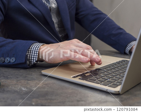 Person in modern office is working on laptop, typing and browsing web. He has blue jacket and button 120791084