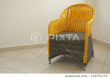 Color blocking wicker armchair made from grey and yellow color plastic faux rattan. Empty woven chair on tiled floor. Patio furniture on beige wall background. Interior mockup with copy space 120791259