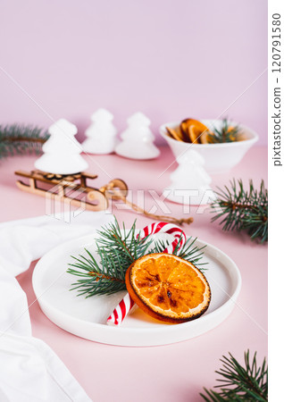 Christmas table setting lollipop, fir tree and dried orange on plate on table vertical view 120791580