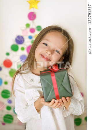 A cute child is holding a New Year's gift in his hands. Bright creative Christmas tree on the wall of the children's room 120791887