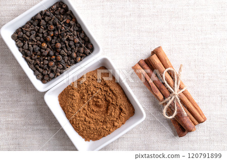 Cassia cinnamon powder and buds in white bowls, with cinnamon sticks tied together in a bundle, on linen fabric, and with empty space for text. Chinese cinnamon, Cinnamomum cassia, used as a spice. 120791899