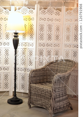 Gray wicker chair against background of wooden light partition close to black floor lamp with white lampshade. Cozy home interior with retro touch 120791908