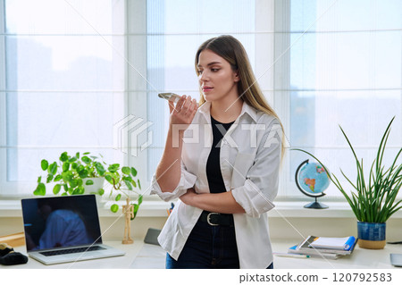 Young woman recording audio message on smartphone, at home 120792583