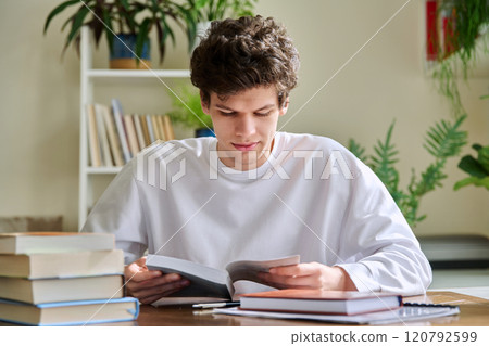 Guy student 19,20 years old studying reading books, sitting at home desk 120792599